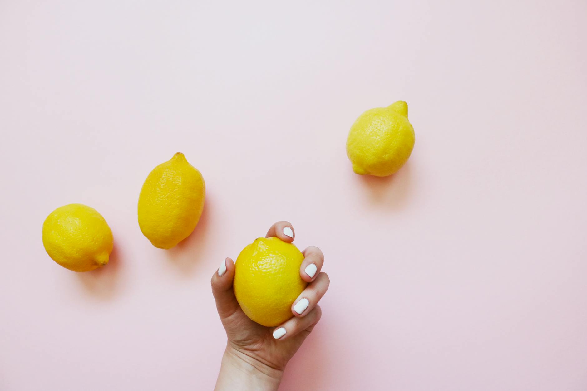 A hand holding a fresh lemon on a soft pink background, symbolizing citrus-inspired pleasure and restoration