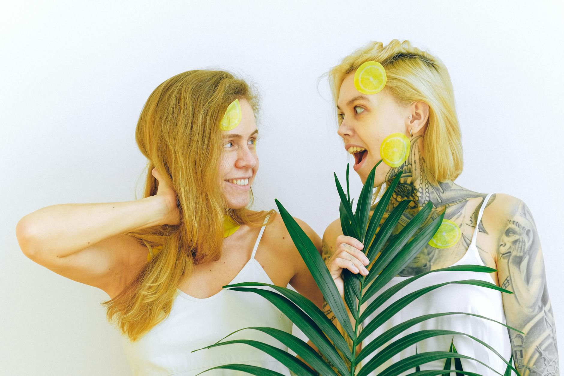 Two women smiling and expressing joy with bright lemons and tropical plant indoors