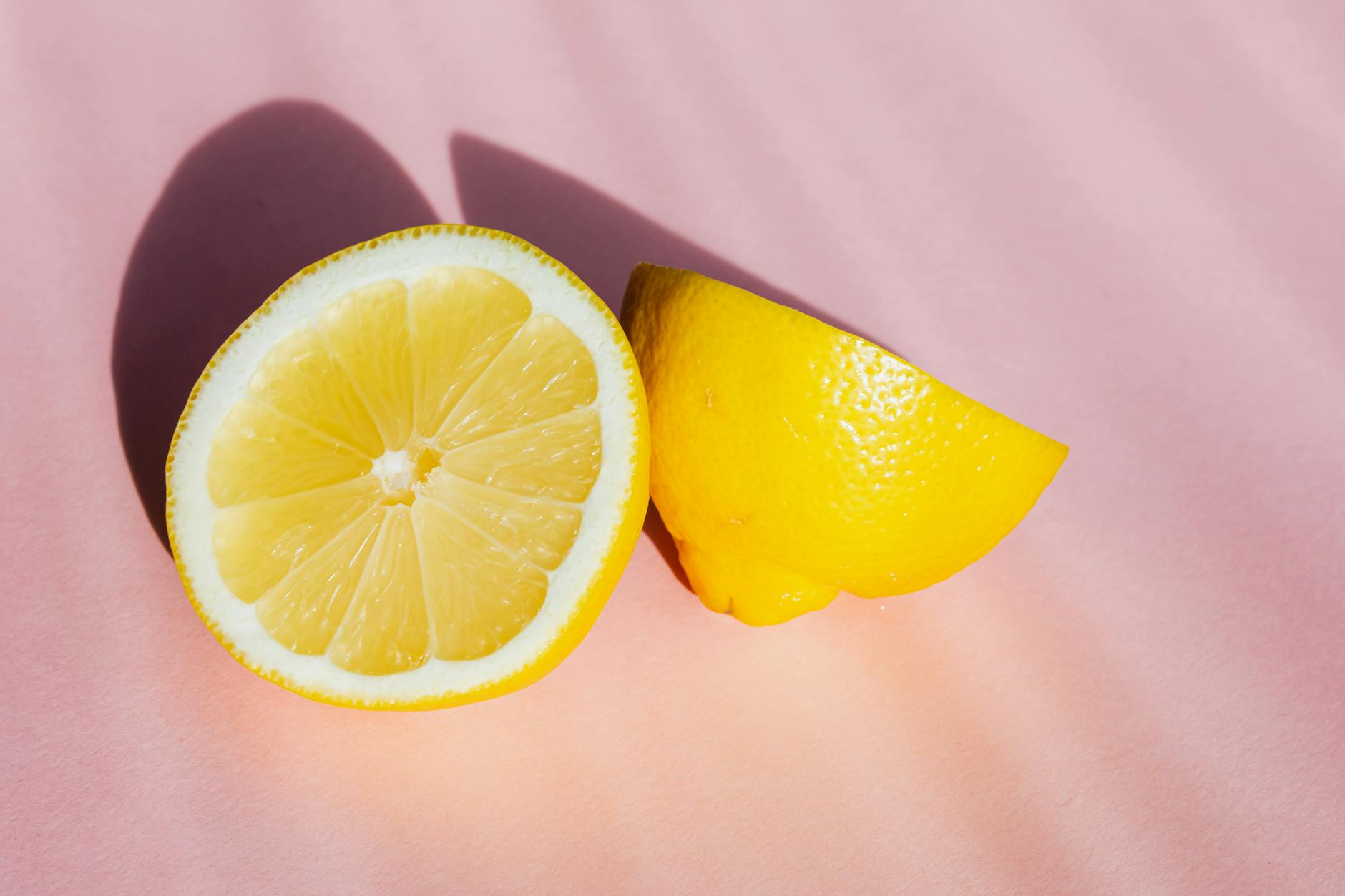 Two fresh lemon halves on a pink background in bright sunlight