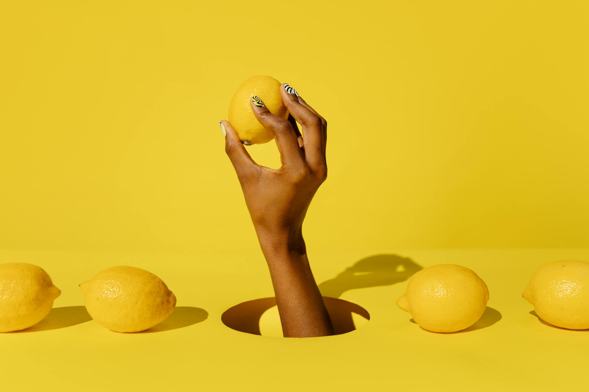 Hand holding a fresh lemon against a yellow background, representing the citrus-inspired design of lemon vibrators