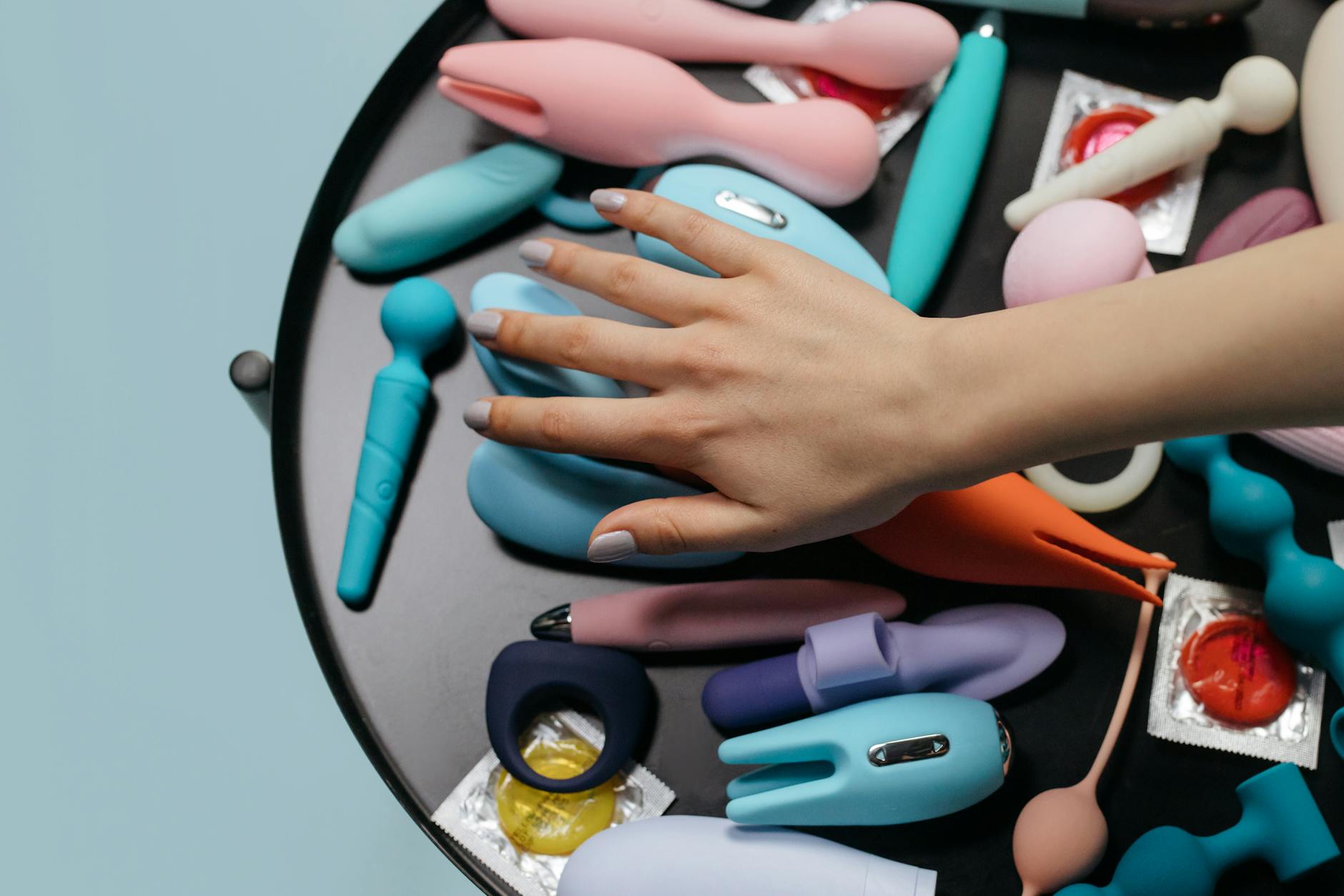 Person holding two colorful vibrators against a purple background, representing pleasure options
