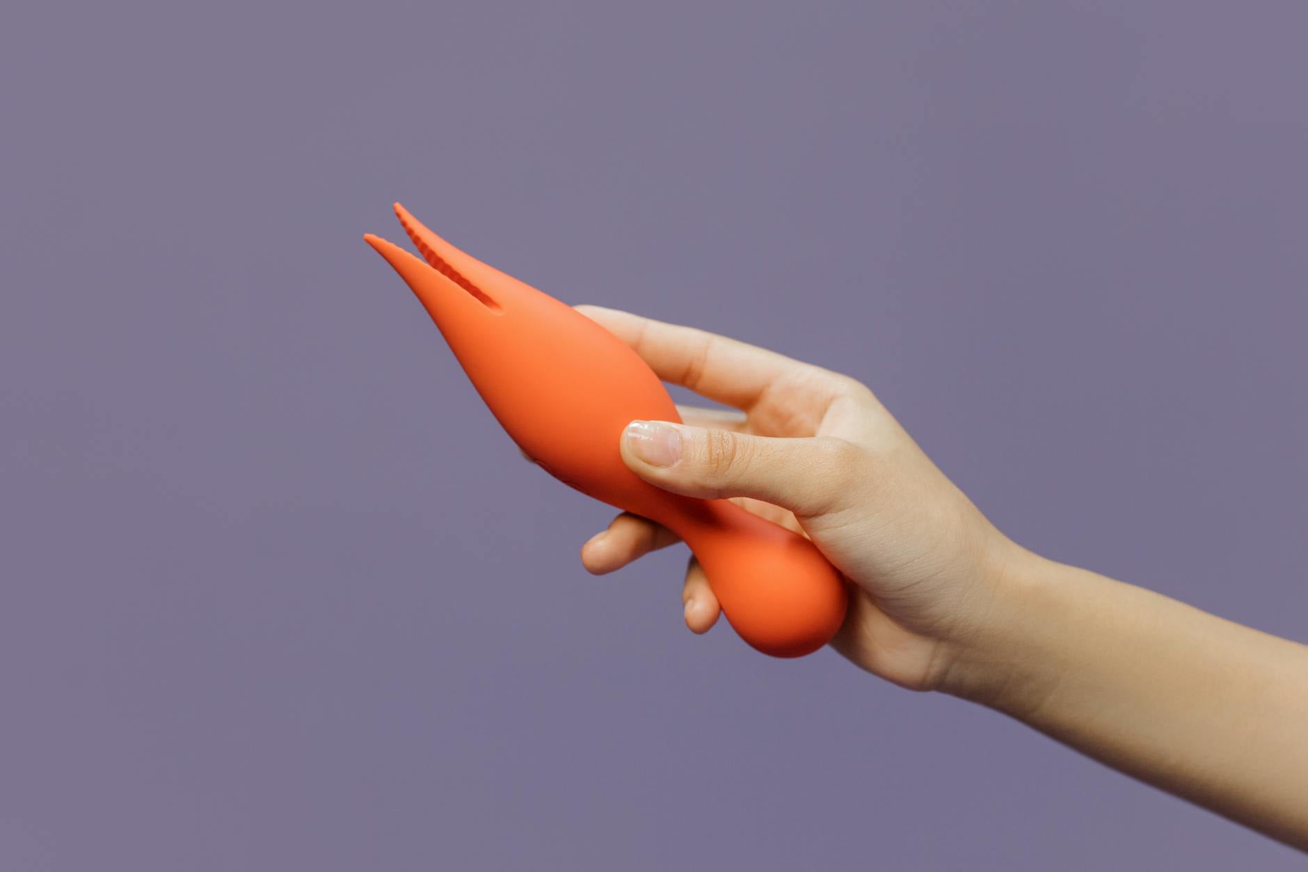 Close-up of hands holding a sleek orange lemon vibrator against a minimalistic purple backdrop, showcasing modern sensuality and pleasure
