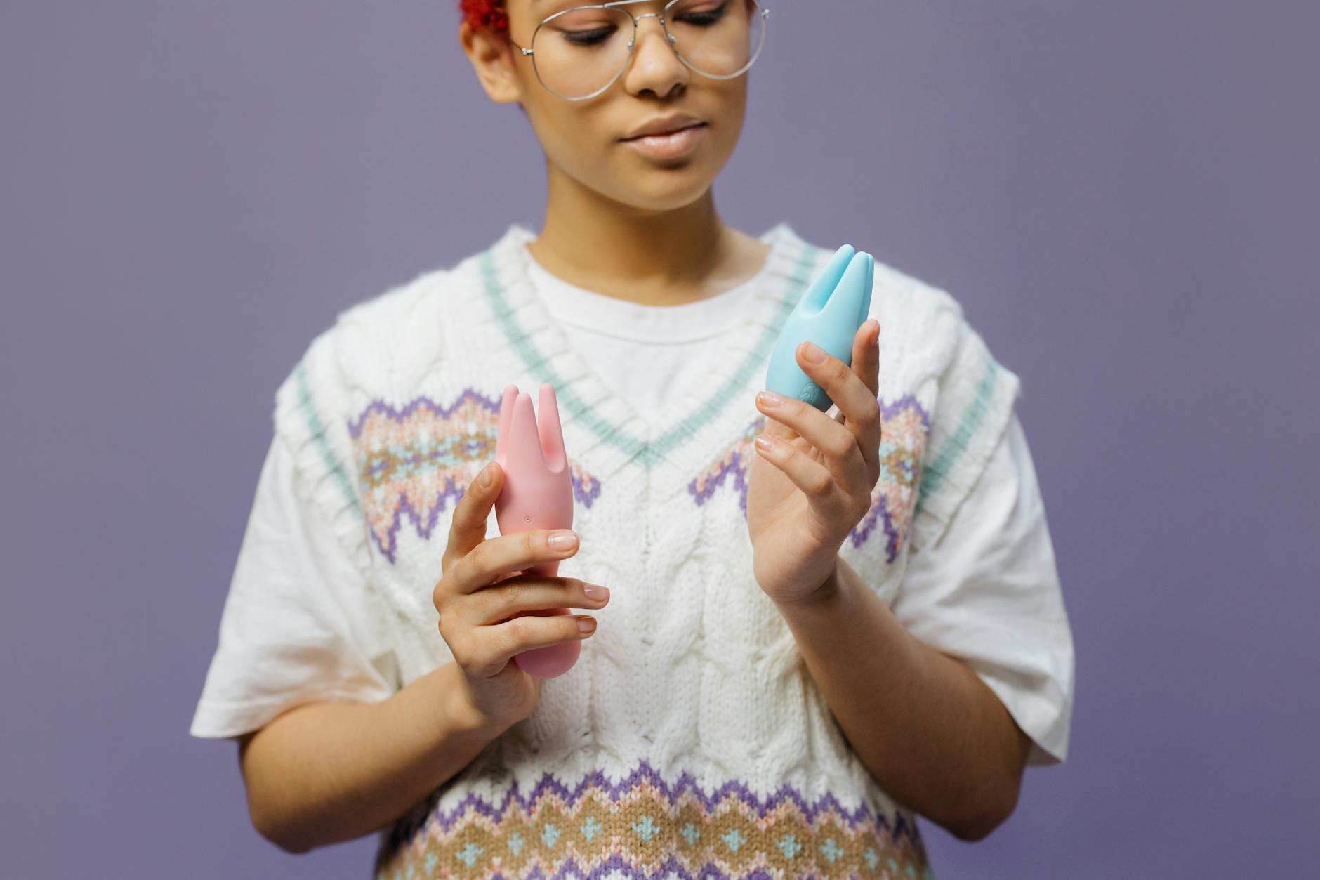 Woman holding blue and pink silicone vibrators in a contemplative manner, representing autonomy over pleasure.