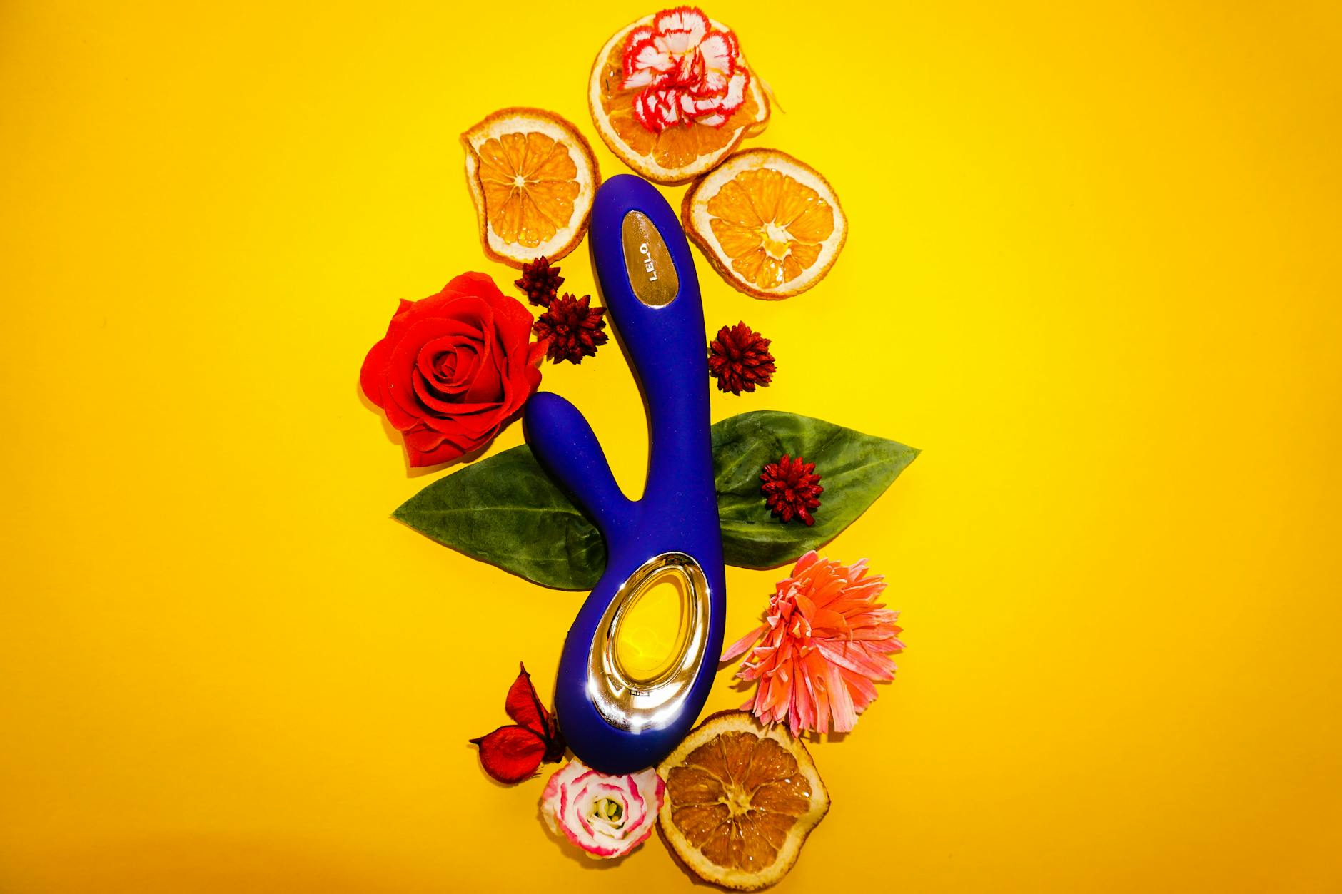 A blue lemon vibrator surrounded by fresh citrus and flowers on a bright yellow background