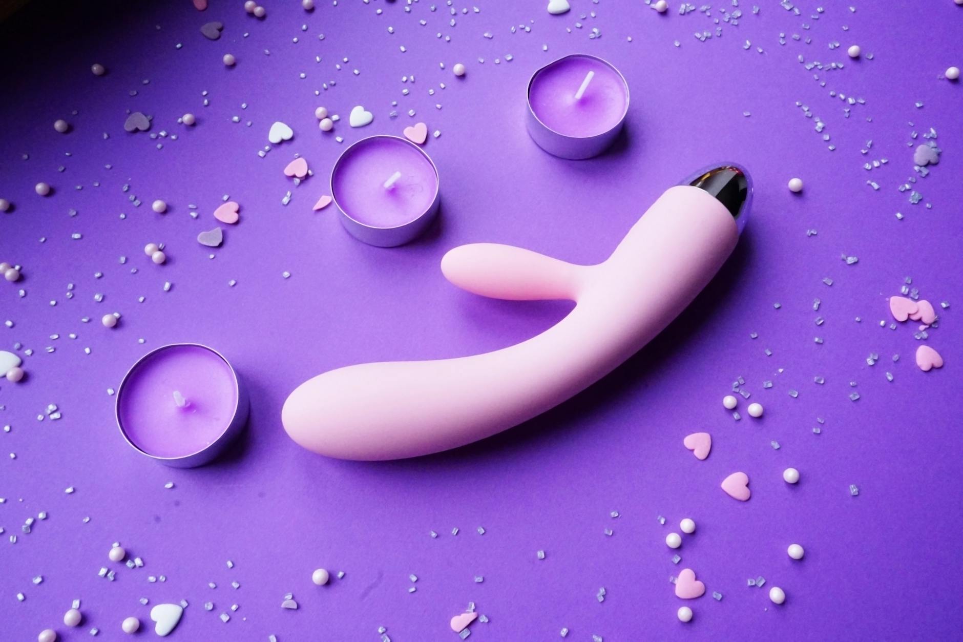 Pink vibrator on purple background with heart confetti and candles for intimate atmosphere